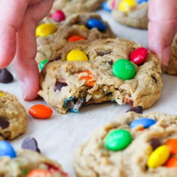 Monster Cookies filled with chocolate chips, nuts and M&Ms on a sheet tray with a bite taken out of one