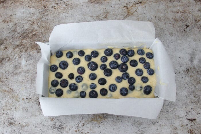 Raw batter in loaf pan with blueberries on top before being baked