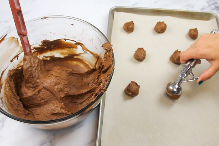 Scooping small rounds of chocolate whoopie pie batter onto a parchment lined baking sheet