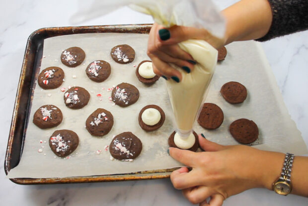Squeezing peppermint buttercream out of a pastry bag onto the baked chocolate whoopie pie cookie