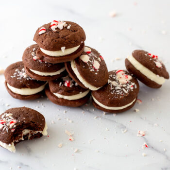 Chocolate peppermint whoopie pies all piled up sitting on a marble platter. One cookie in front has a bit taken out of it