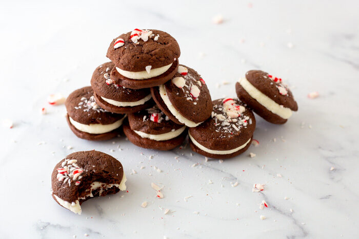 Chocolate peppermint whoopie pies piled up sitting on a marble platter. One cookie in front has a bit taken out of it