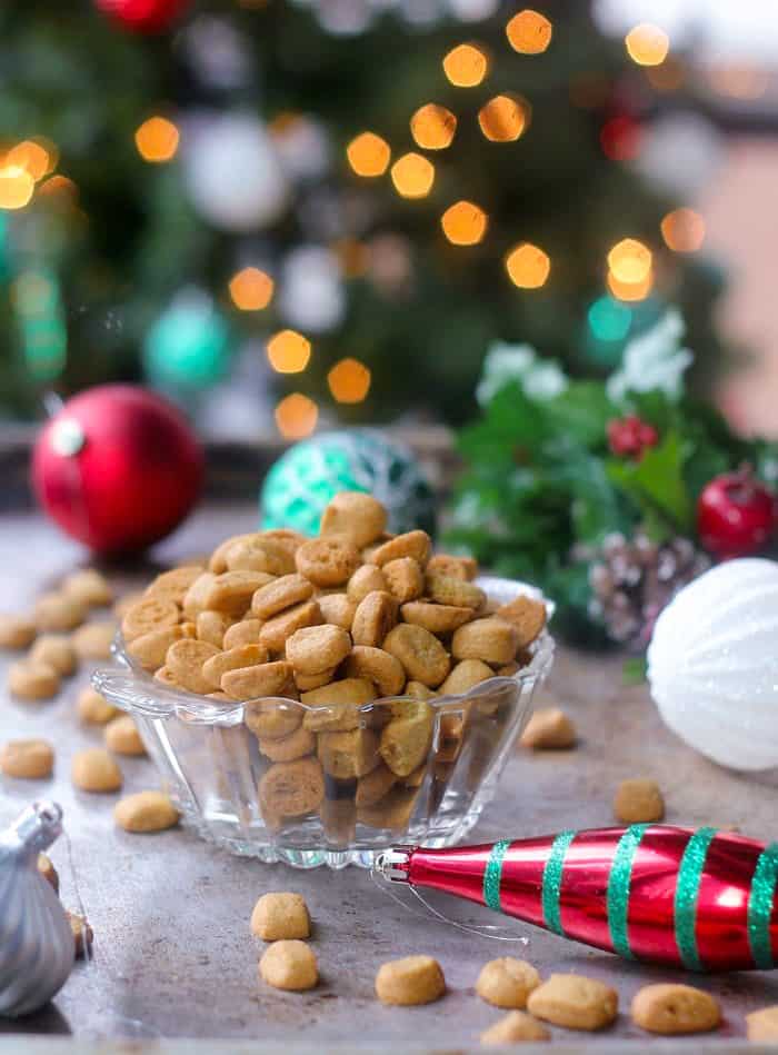 Bowl of peppernuts in a candy dish with christmas ornaments laying around and christmas lights in the background