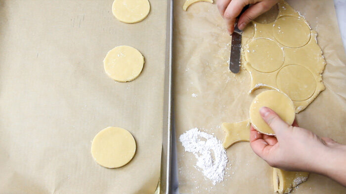 cookie dough that has been cut into rounds are being transferred onto a parchment lined baking sheet