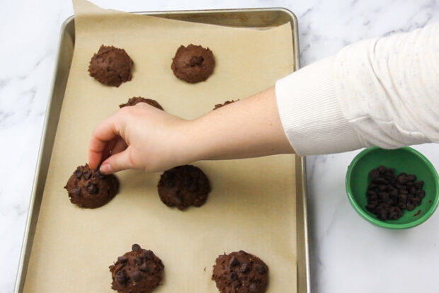 Topping each mound of cookie dough with more chocolate chips before baking