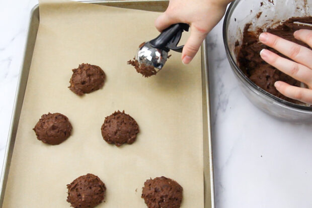 Scooping mounds of spicy chocolate cookie dough onto a parchment lined baking sheet