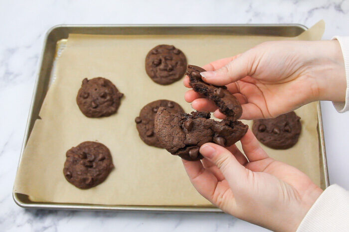 Tray of baked spicy chocolate cookies and one is being held and broken open, showing the gooey middle