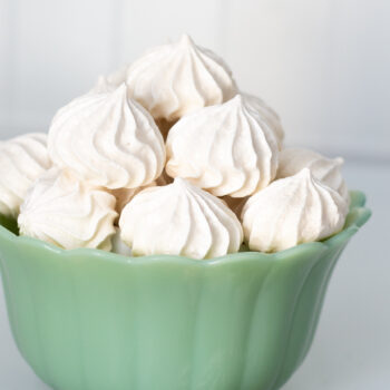 Meringue kisses piled up in a green bowl on a white background