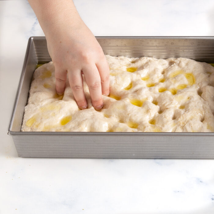 dimpling focaccia dough with fingertips
