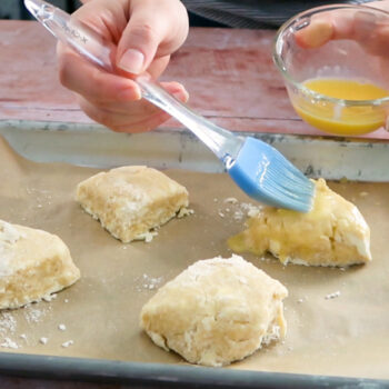 Egg wash being brushed on a tray of scones with a pastry brush