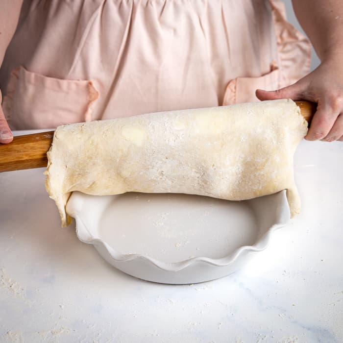 transferring pie dough from the rolling pin into the pie plate