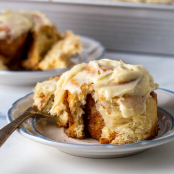 sourdough cinnamon roll on a plate with a bite taken out of it showing the inside