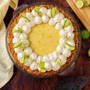 Overhead view of a classic key lime pie that is decorated with piped whipped cream and lime wedges