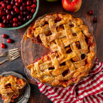 cranberry apple pie with a slice cut out of it and a bowl of cranberries