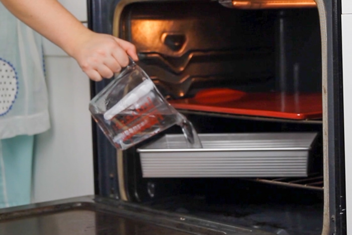 Pouring hot water into a roasting pan to preheat in the oven. There is also a baking stone in the oven to preheat. 