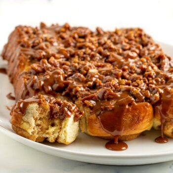 Platter of pecan caramel sticky buns, one has a bit taken out of it and caramel is dripping down