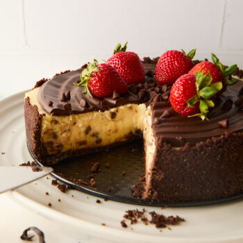 chocolate chip cheesecake topped with ganache and fresh strawberries with a slice taken out