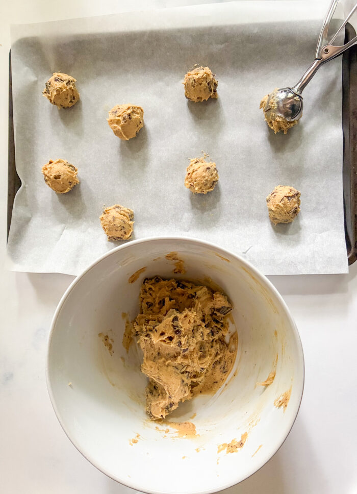 small cookie dough mounds being scooped onto a baking sheet