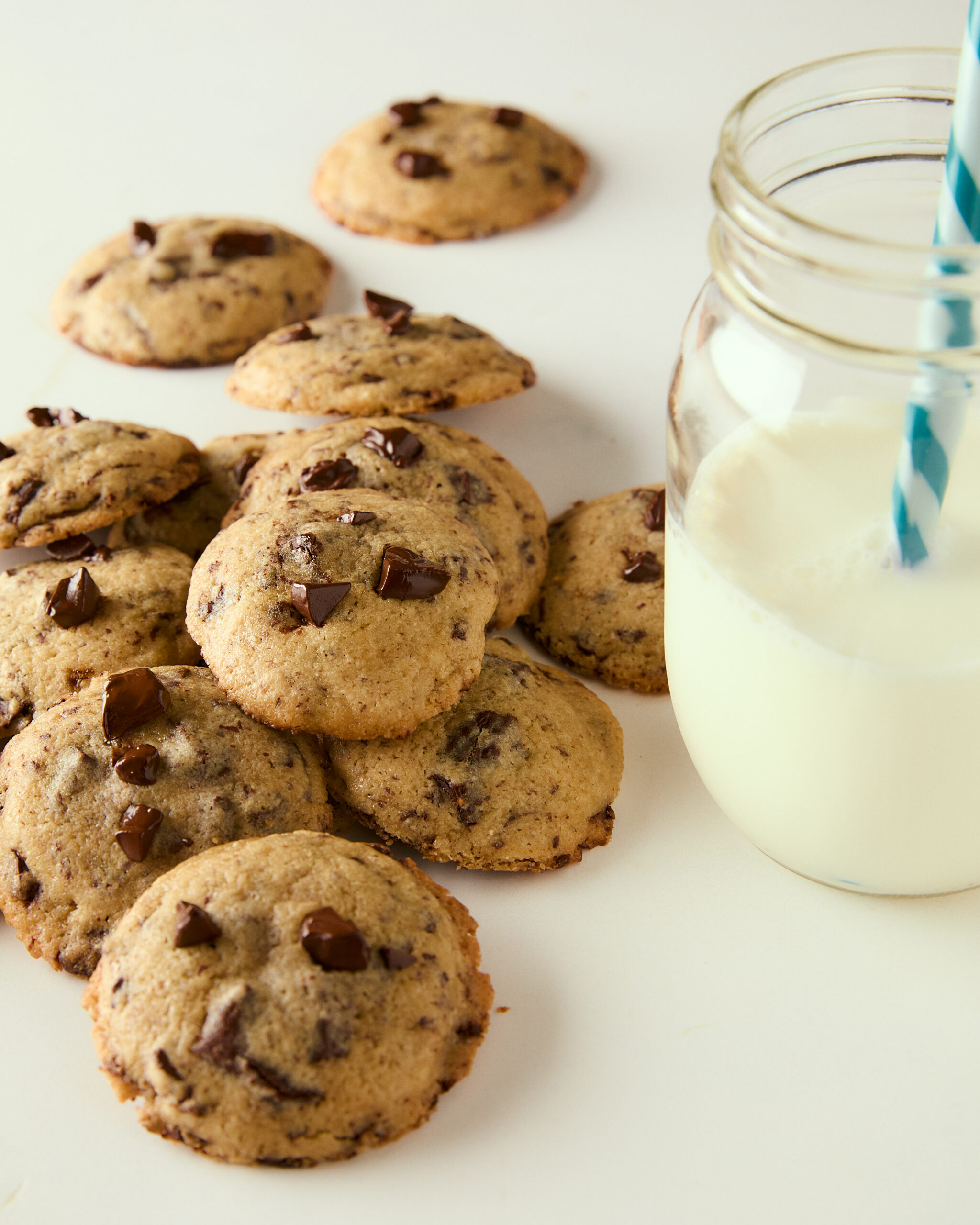 mini chocolate chip cookies piled on a counter with a glass of milk