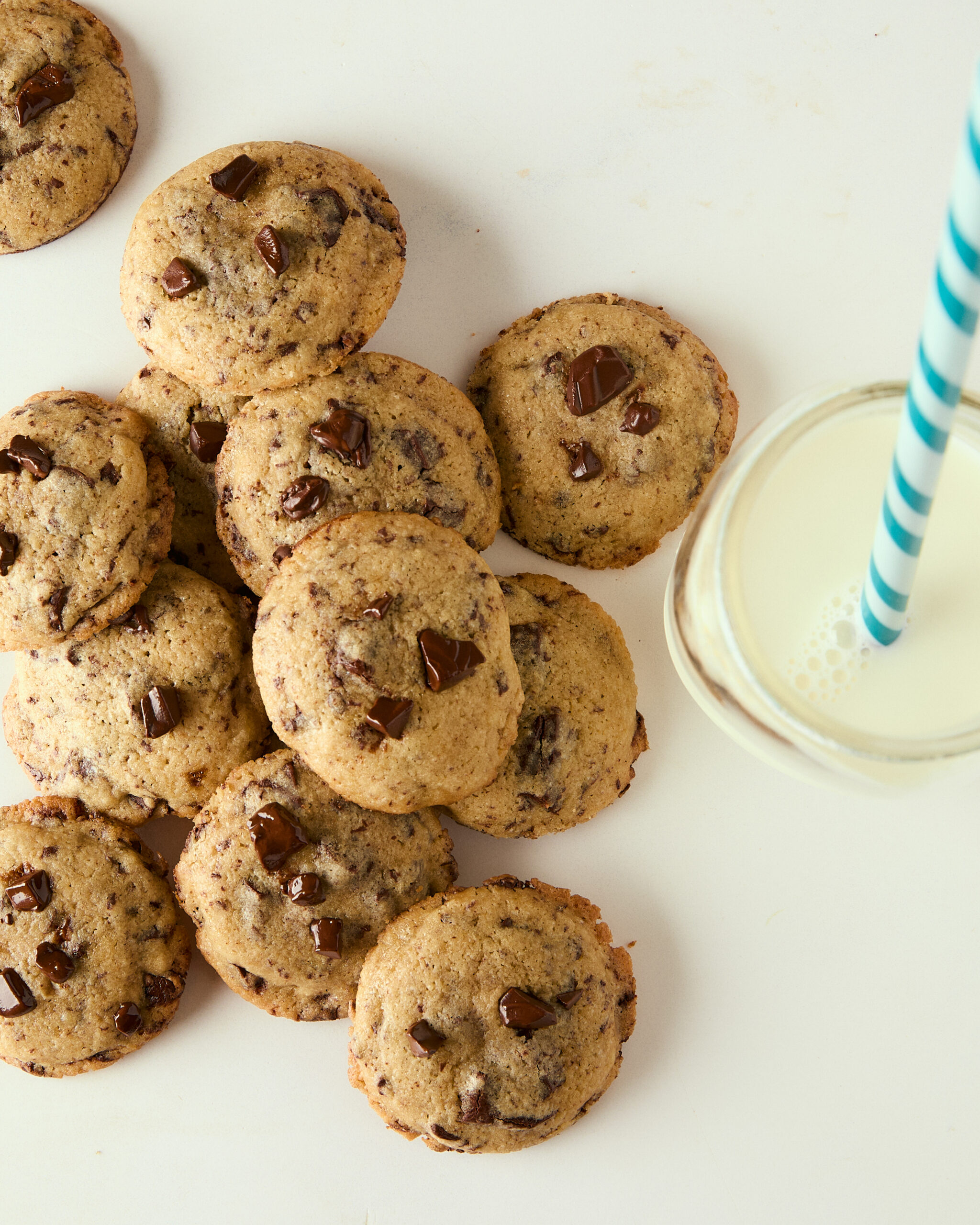 mini chocolate chip cookies piled on a counter with a glass of milk