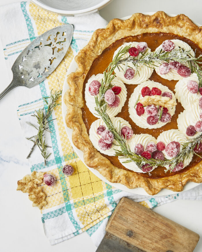 A whole creamy pumpkin pie topped with whipped cream and sugared rosemary and cranberries