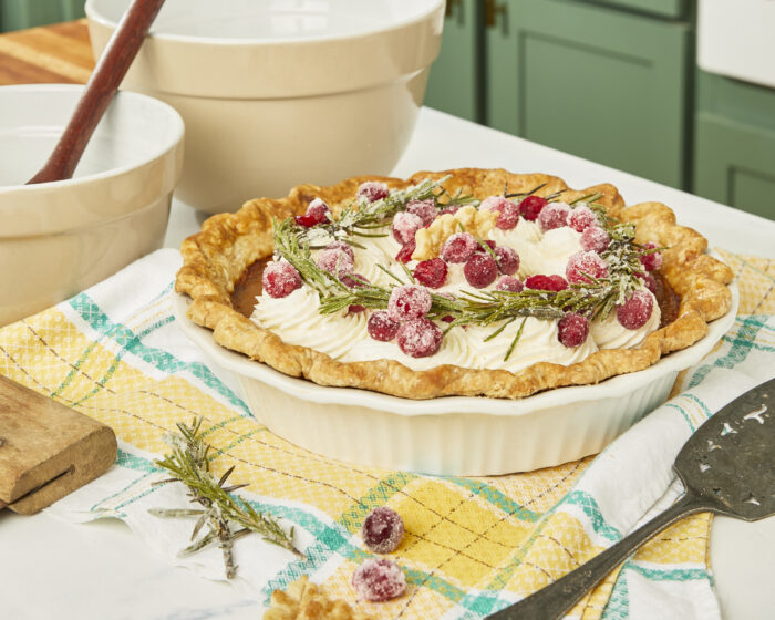 Creamy pumpkin pie decorated with sugared rosemary, cranberries, and whipped cream