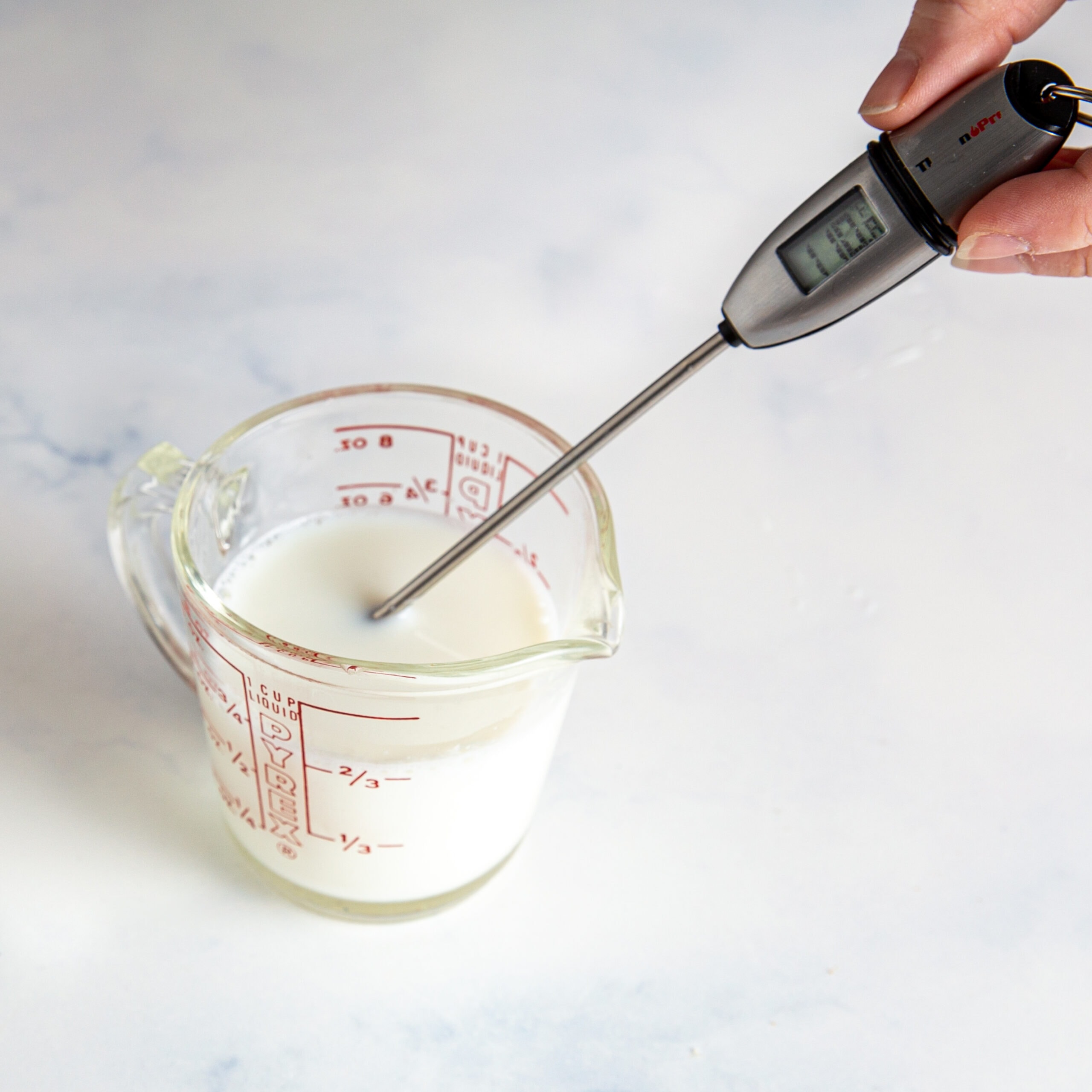A thermometer taking the temperature of milk in a measuring cup