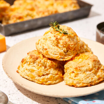 Garlic cheddar biscuits on a plate with a pan of biscuits behind