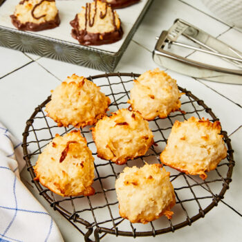 Classic coconut macaroons on a wire rack with chocolate drizzled coconut macaroons in the background