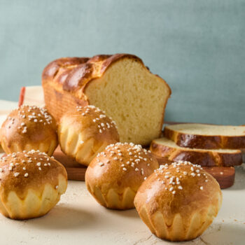 A cut loaf of brioche with brioche rolls topped with sugar nibs