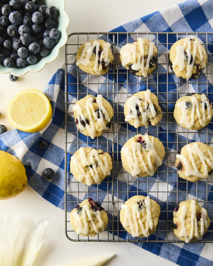 These blueberry cookies are soft, fluffy, and tender and are topped with a tangy lemon glaze! Perfect for summer gatherings! blueberry cookies with lemon glaze on a wire rack