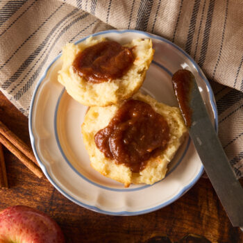 Homemade apple butter spread over a biscuit on a plate