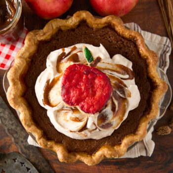 apple butter pie topped with whipped cream and a painted piece of pie dough to look like an apple