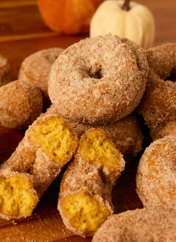 pumpkin donuts on a table, one split open to see orange donut inside